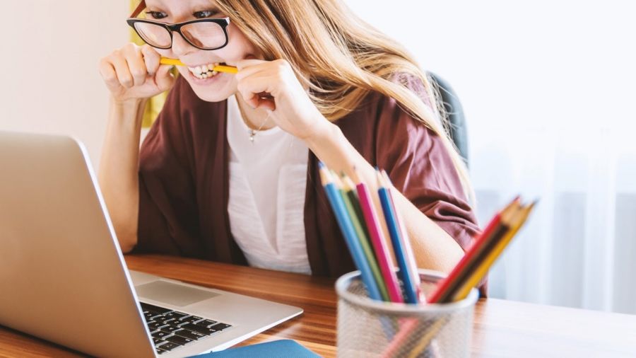 girl at desk biting her pencil while looking at laptop 
