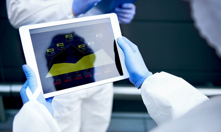 A person with surgical gloves on holding a tablet with data displayed