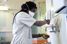 A medical professional wearing a face mask and washing their hands under a faucet