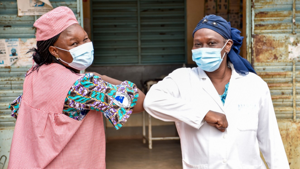 two healthcare workers in PPE bumping elbows in greeting 